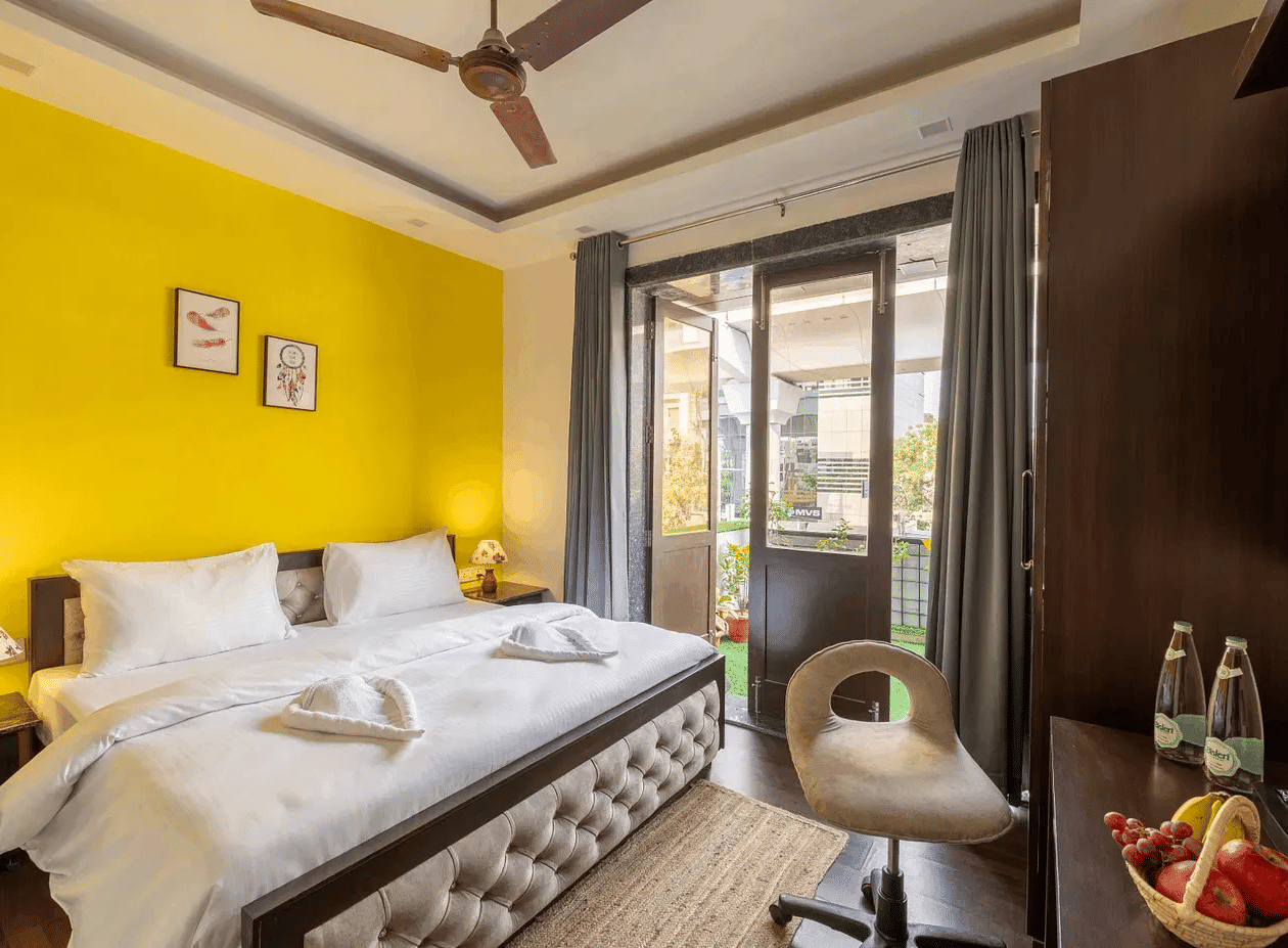 A brightly lit yellow-walled hotel room with a double bed and a large window - Lime Boutique Bed & Breakfast | Nehru Place Metro